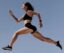 Energetic woman in athletic wear leaping against clear blue sky, symbolizing freedom and fitness.